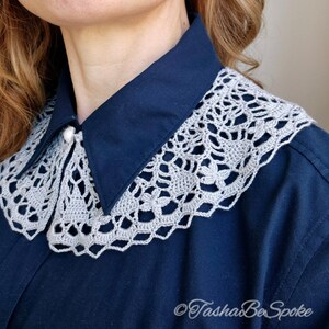 May include: A gray crocheted collar with a delicate floral pattern, worn over a navy blue shirt.