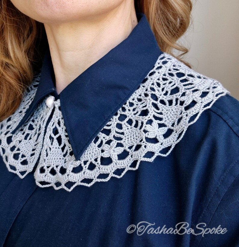 May include: A gray crocheted collar with a delicate floral pattern, worn over a navy blue shirt.