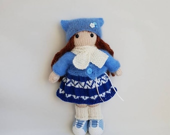 May include: A knitted doll wearing a blue hat, blue sweater, white scarf, blue and white skirt, and blue and white shoes.
