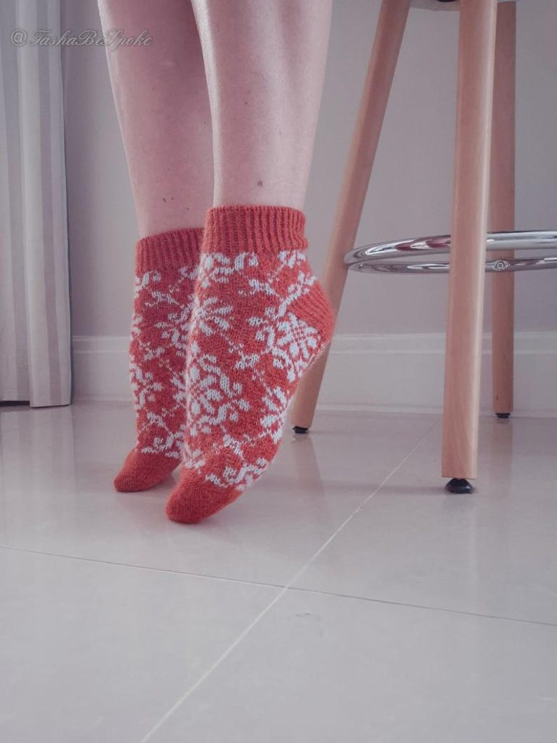 May include: A pair of orange and white patterned socks. The socks have a snowflake design and are worn on the feet. The socks are made of a knitted material. The image is taken indoors.