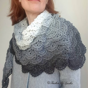 May include: A crocheted shawl with a gradient of white, grey, and black. The shawl has a delicate lace pattern and a scalloped edge.