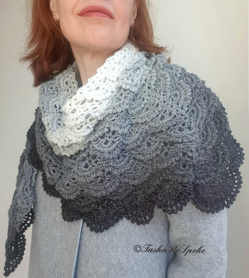 May include: A crocheted shawl with a gradient of white, grey, and black. The shawl has a delicate lace pattern and a scalloped edge.