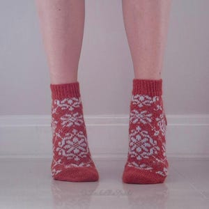 May include: A pair of red knitted socks with a white snowflake pattern. The socks are ankle-length and have a ribbed cuff. The socks are worn on a person's feet.