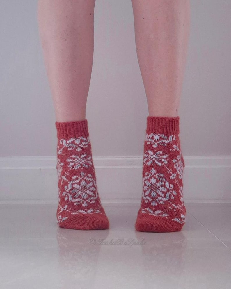 May include: A pair of red knitted socks with a white snowflake pattern. The socks are ankle-length and have a ribbed cuff. The socks are worn on a person's feet.