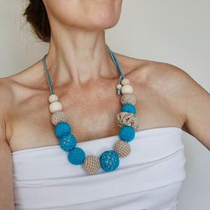 Op de afbeelding: Een handgemaakte ketting met een mix van kralen. De ketting heeft lichtblauwe, beige en houten kralen. De kralen zijn in een cirkelvormig patroon gerangschikt, wat een uniek accessoire cre&euml;ert. De ketting is een opvallend sieraad.