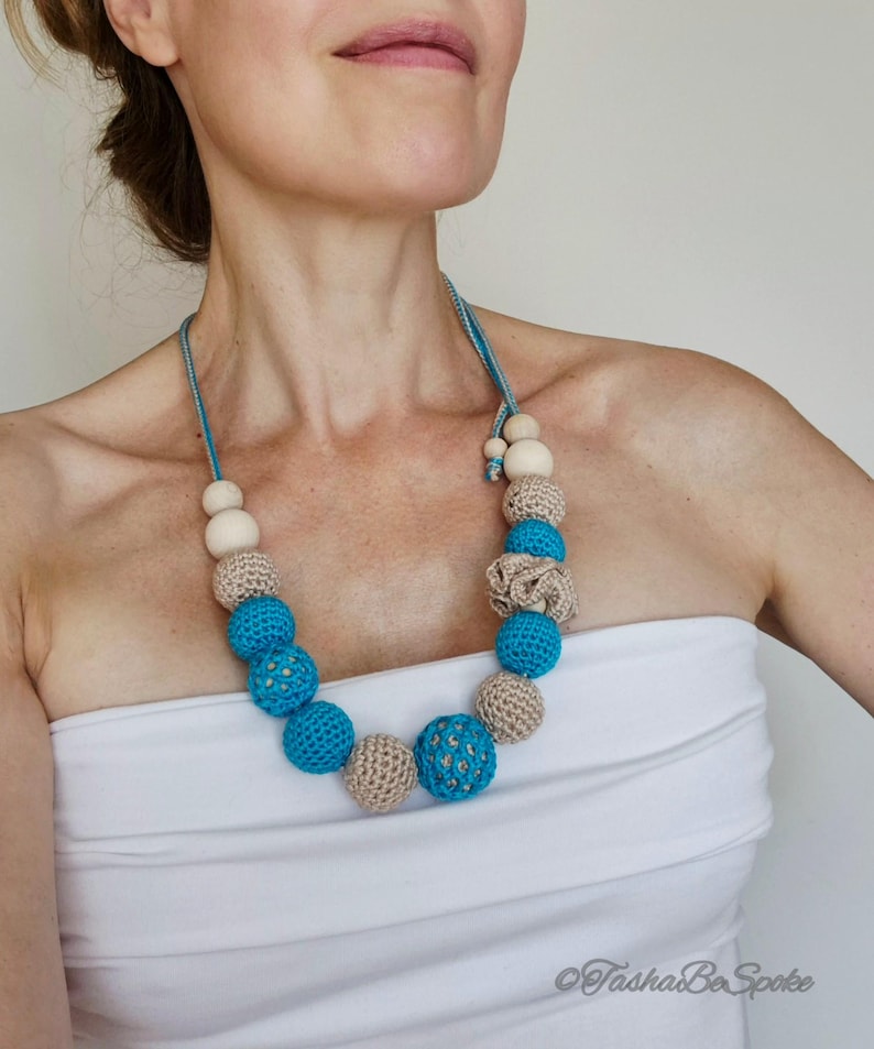 Op de afbeelding: Een handgemaakte ketting met een mix van kralen. De ketting heeft lichtblauwe, beige en houten kralen. De kralen zijn in een cirkelvormig patroon gerangschikt, wat een uniek accessoire cre&euml;ert. De ketting is een opvallend sieraad.