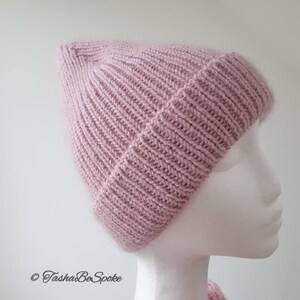 K&ouml;nnte beinhalten: Eine rosa gestrickte M&uuml;tze mit Rippenstruktur. Die M&uuml;tze sitzt auf einem wei&szlig;en Mannequin-Kopf.
