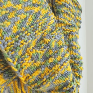 May include: A chunky knit scarf with a fringe in shades of gray, green, and yellow.