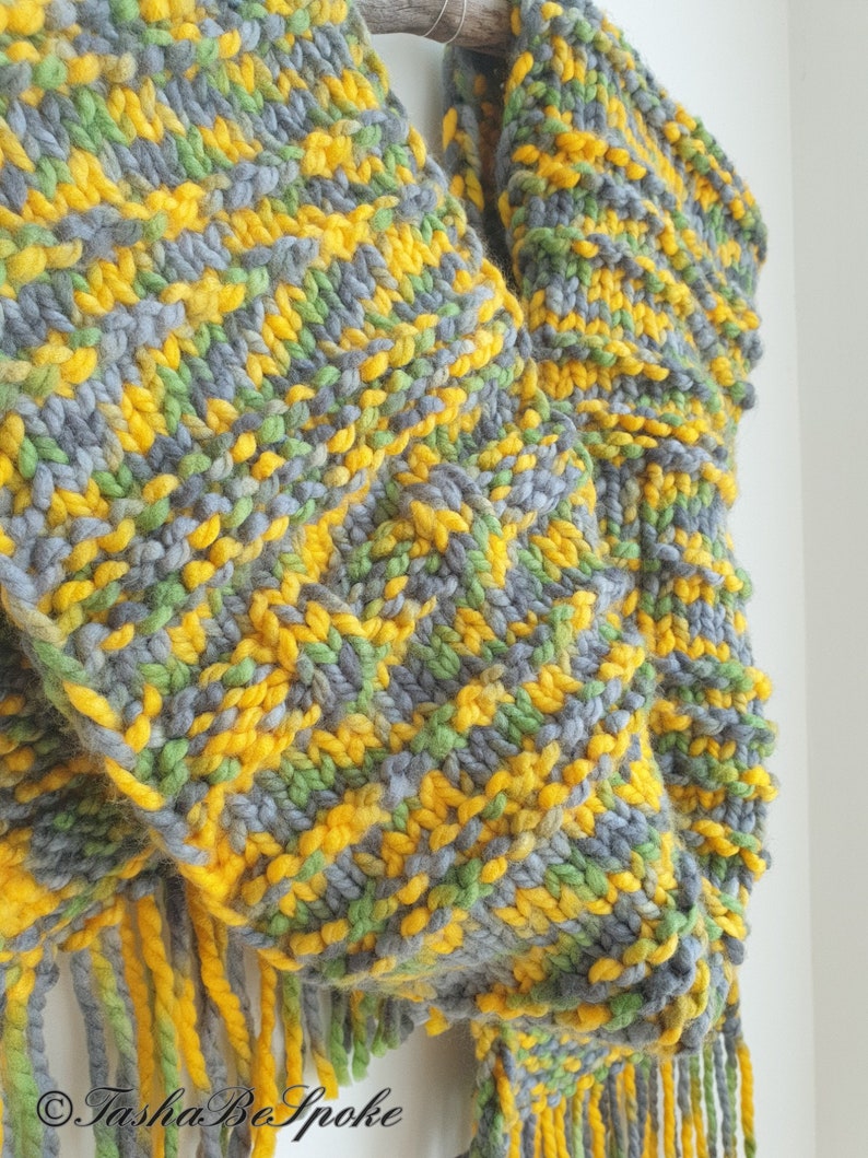 May include: A chunky knit scarf with a fringe in shades of gray, green, and yellow.