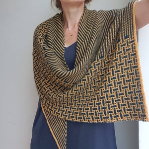 Pode incluir: Um chal triangular com um padr&atilde;o geom&eacute;trico em tons de amarelo mostarda e verde escuro. O chal &eacute; tricotado com um fio fino e tem uma franja delicada.
