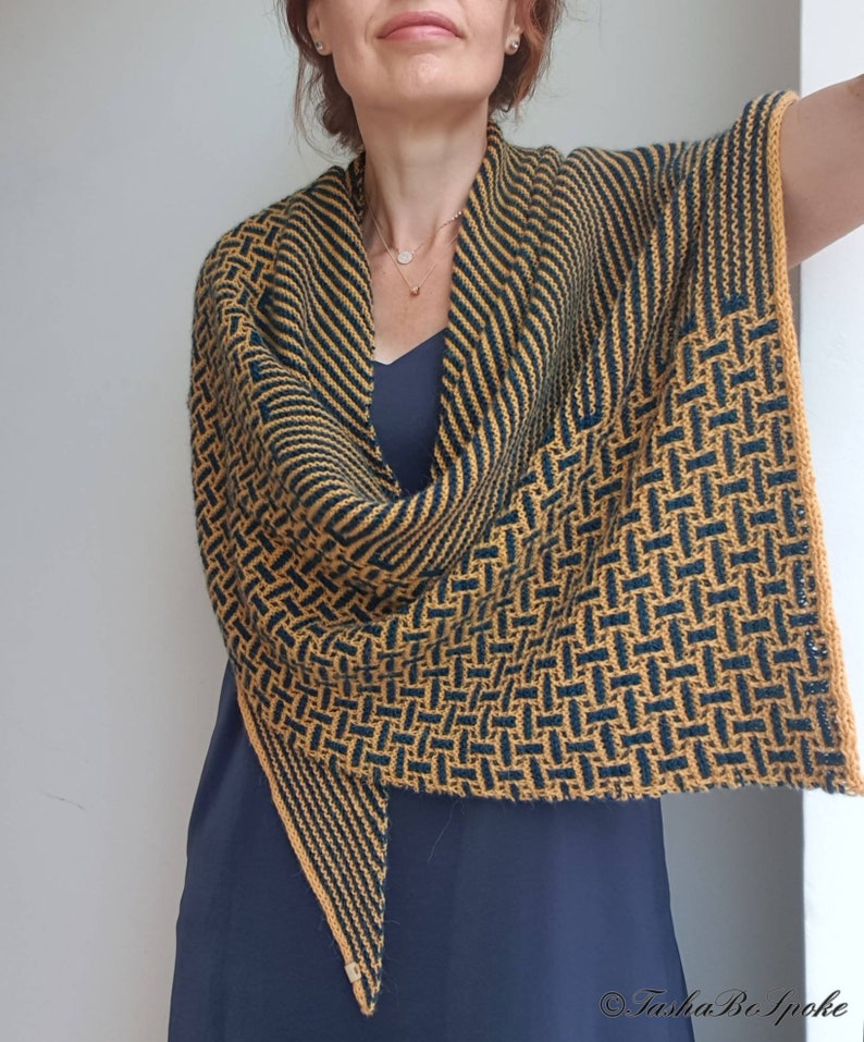 Pode incluir: Um chal triangular com um padr&atilde;o geom&eacute;trico em tons de amarelo mostarda e verde escuro. O chal &eacute; tricotado com um fio fino e tem uma franja delicada.