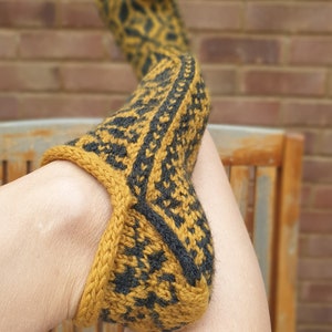 May include: A pair of knitted slippers with a black and gold geometric pattern. The slippers are folded over and the heel is visible.