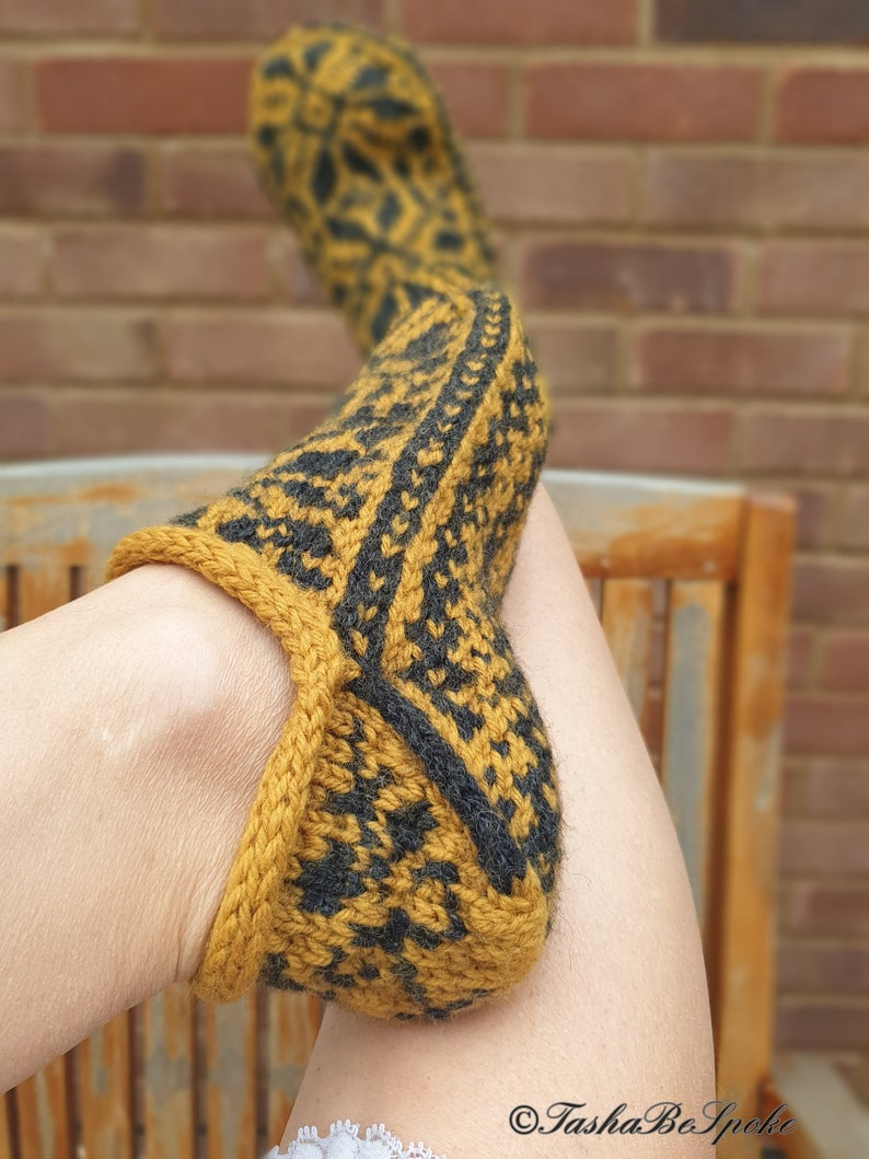 May include: A pair of knitted slippers with a black and gold geometric pattern. The slippers are folded over and the heel is visible.