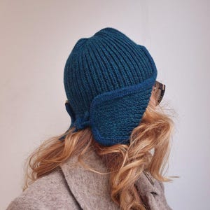 K&ouml;nnte beinhalten: Eine tealblaue Strickm&uuml;tze mit umgeschlagenem Rand und einem einzigartigen Ohrenschutz-Design. Die M&uuml;tze ist aus einem weichen, warmen Material gefertigt und perfekt f&uuml;r kaltes Wetter.
