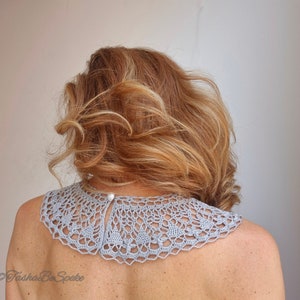 May include: A light gray crocheted collar with a delicate pattern. The collar is worn by a person with long, wavy, light brown hair.