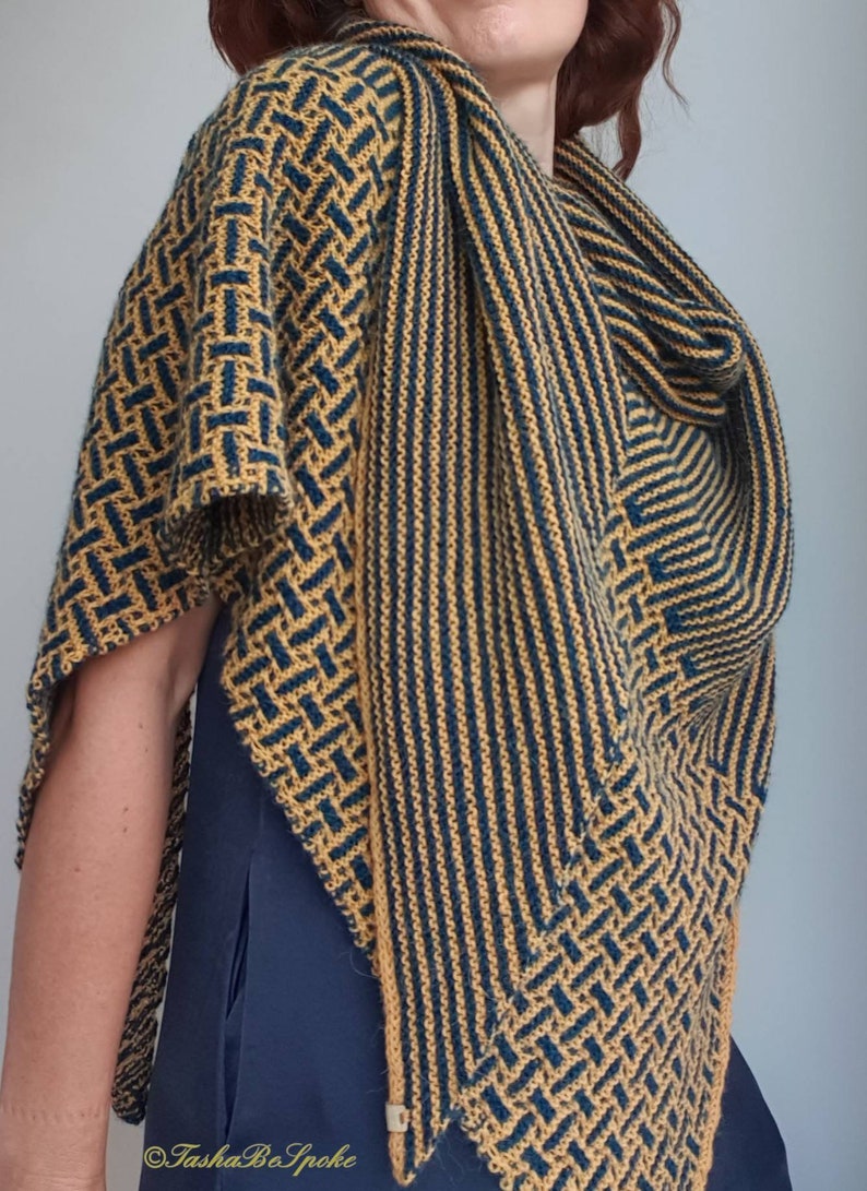 Pode incluir: Um chal triangular com um padr&atilde;o geom&eacute;trico em tons de amarelo mostarda e azul turquesa. O chal &eacute; tricotado com um fio fino e tem uma franja delicada.