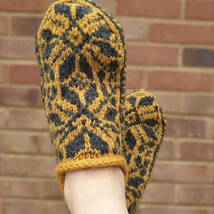 May include: A pair of knitted slippers with a geometric pattern in mustard yellow and black. The slippers are worn on a person's feet.