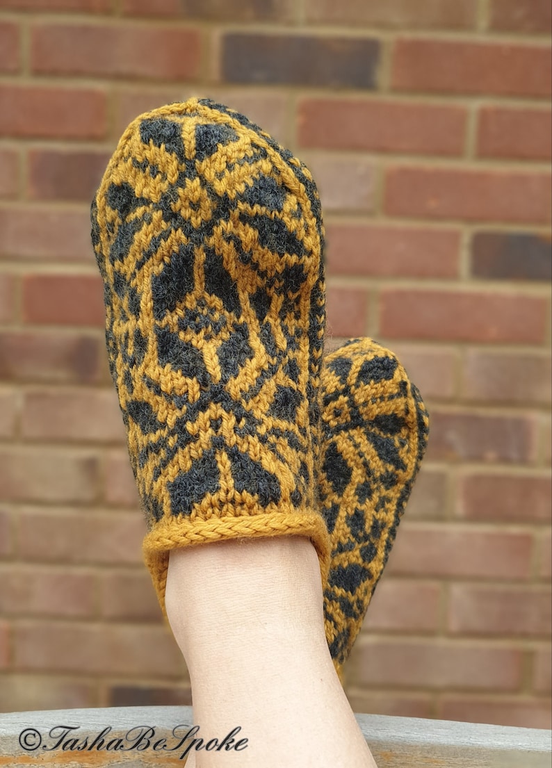 May include: A pair of knitted slippers with a geometric pattern in mustard yellow and black. The slippers are worn on a person's feet.