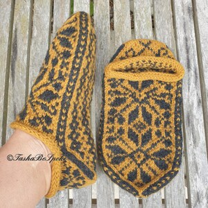 May include: A pair of knitted slippers in a mustard yellow and black color scheme with a geometric pattern. The slippers are made with a soft yarn and have a comfortable fit.