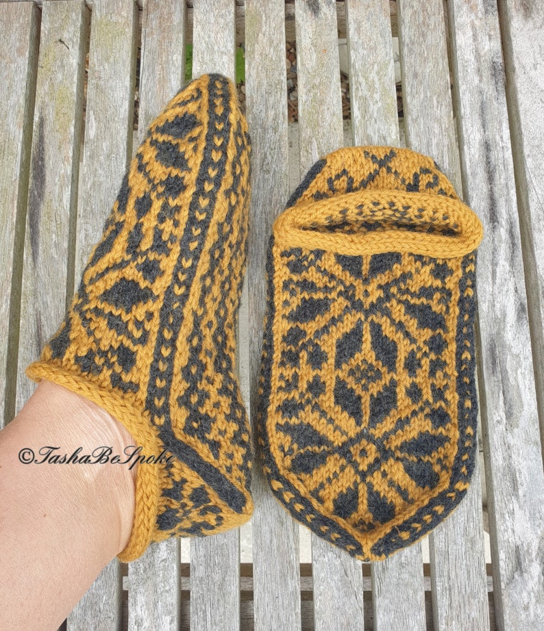 May include: A pair of knitted slippers in a mustard yellow and black color scheme with a geometric pattern. The slippers are made with a soft yarn and have a comfortable fit.