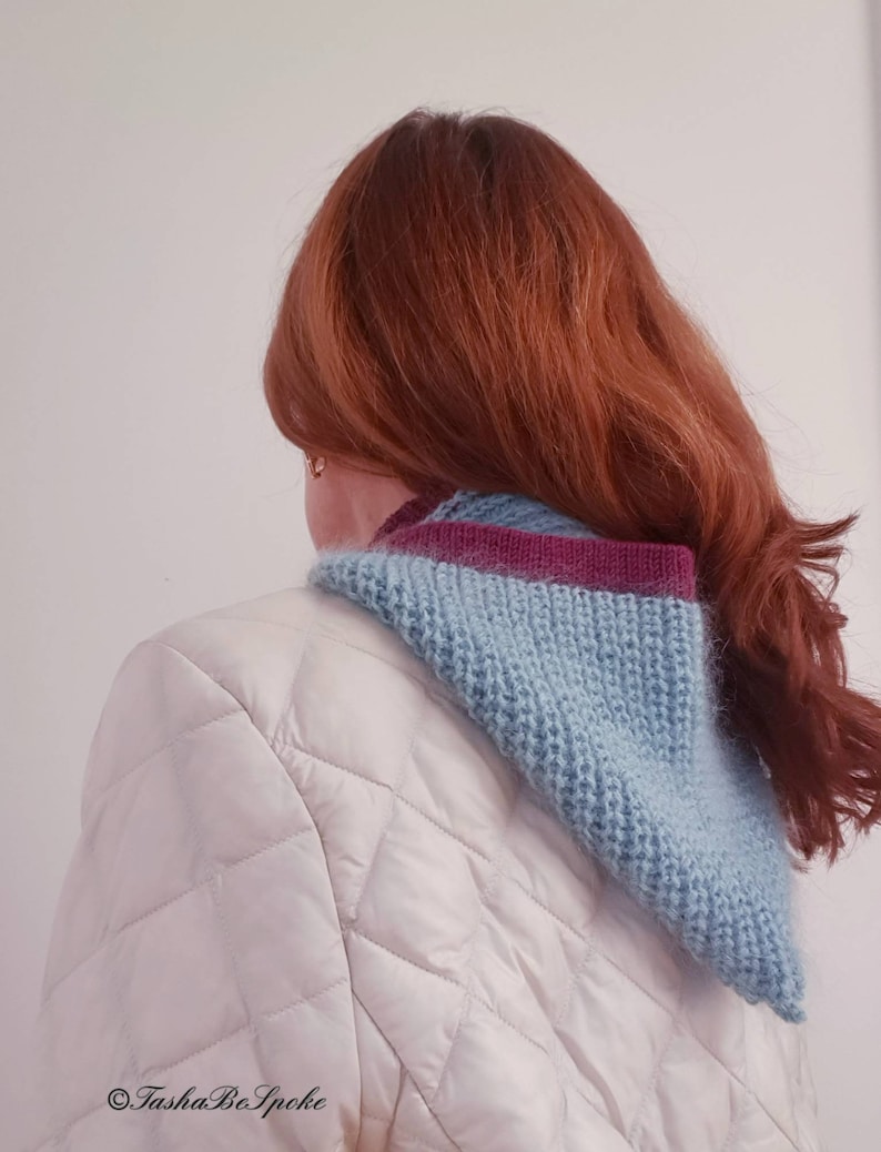 Pu&ograve; includere: Un collo a maglia blu chiaro e viola. La sciarpa &egrave; indossata sopra una giacca trapuntata bianca. La modella ha lunghi capelli rossi. La sciarpa &egrave; a forma di triangolo e sembra fatta a mano.