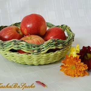 Puede incluir: Una cesta tejida de color verde claro llena de manzanas rojas. La cesta tiene un dise&ntilde;o trenzado. Junto a la cesta hay flores naranjas, amarillas y rojas. La imagen est&aacute; sobre un fondo blanco.