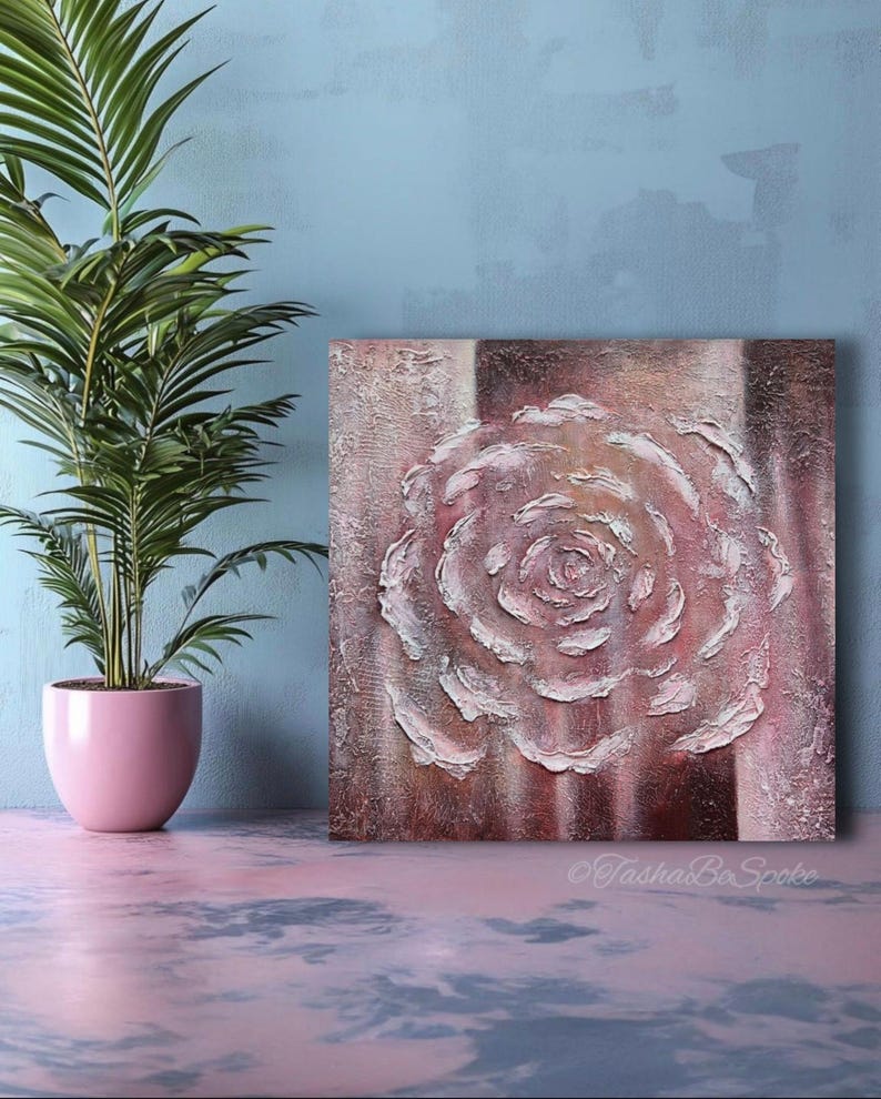 May include: Square canvas art with a textured, raised-relief rose in white and pink hues. The artwork is set against a backdrop of brown and pink vertical stripes. A potted palm plant in a pink pot is on the left.
