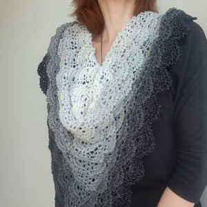 May include: A grey and black crocheted shawl with a scalloped edge. The shawl is made with a gradient yarn that transitions from light grey to dark grey.