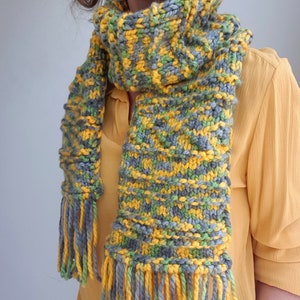 May include: A knitted scarf with a yellow, green, and gray color pattern. The scarf has long fringe tassels on both ends.