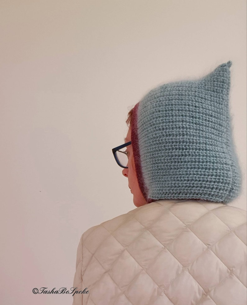 Pu&ograve; includere: Un cappello all'uncinetto azzurro con la parte superiore a punta. Il cappello ha un aspetto strutturato e viene indossato sopra una testa con gli occhiali. La persona indossa una giacca trapuntata bianca. L'immagine include il testo "Tasha BoSpoke".