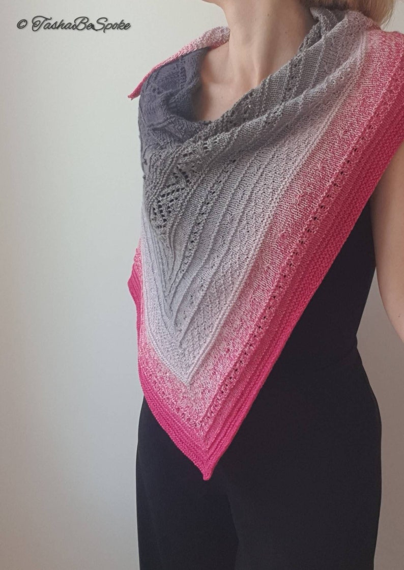 May include: A triangular shawl with a gradient of grey, white, and pink. The shawl is knitted with a delicate lace pattern.