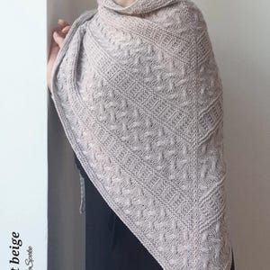 May include: A light beige knitted shawl with a cable stitch pattern. The shawl is draped over a person's shoulders.