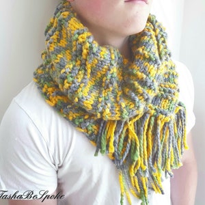 May include: A gray, yellow, and green knitted cowl with long fringe. The cowl is worn by a person.