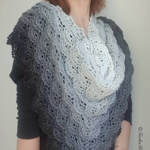 May include: A grey and white crochet shawl with a delicate lace pattern. The shawl is draped around a person's shoulders and neck.