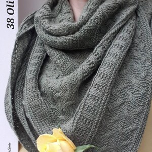 May include: A green knitted shawl with a cable knit pattern. The shawl is draped over a person's shoulders and a yellow rose is in the foreground.