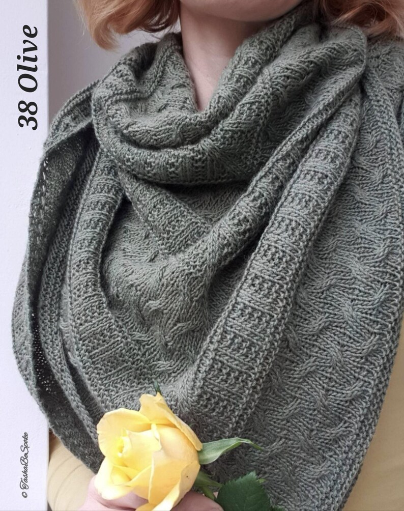 May include: A green knitted shawl with a cable knit pattern. The shawl is draped over a person's shoulders and a yellow rose is in the foreground.