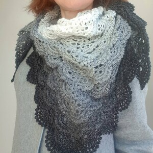 May include: A black and white ombre crochet shawl with a delicate lace pattern. The shawl is draped around a person's neck and shoulders.