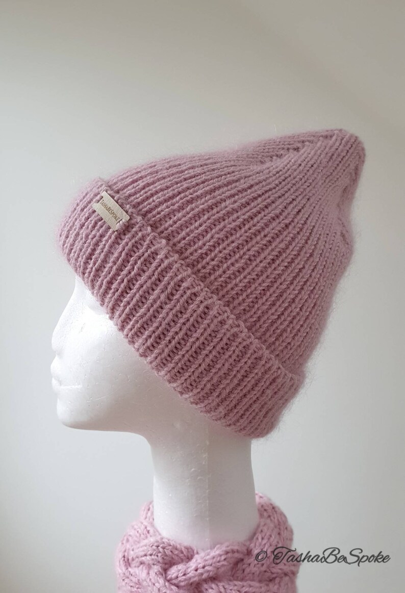 K&ouml;nnte beinhalten: Eine rosafarbene Strickm&uuml;tze mit einem kleinen Etikett mit der Aufschrift "TashaBeSpoke".