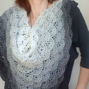 May include: A grey and black crocheted shawl with a scalloped edge. The shawl is draped around a person's shoulders.