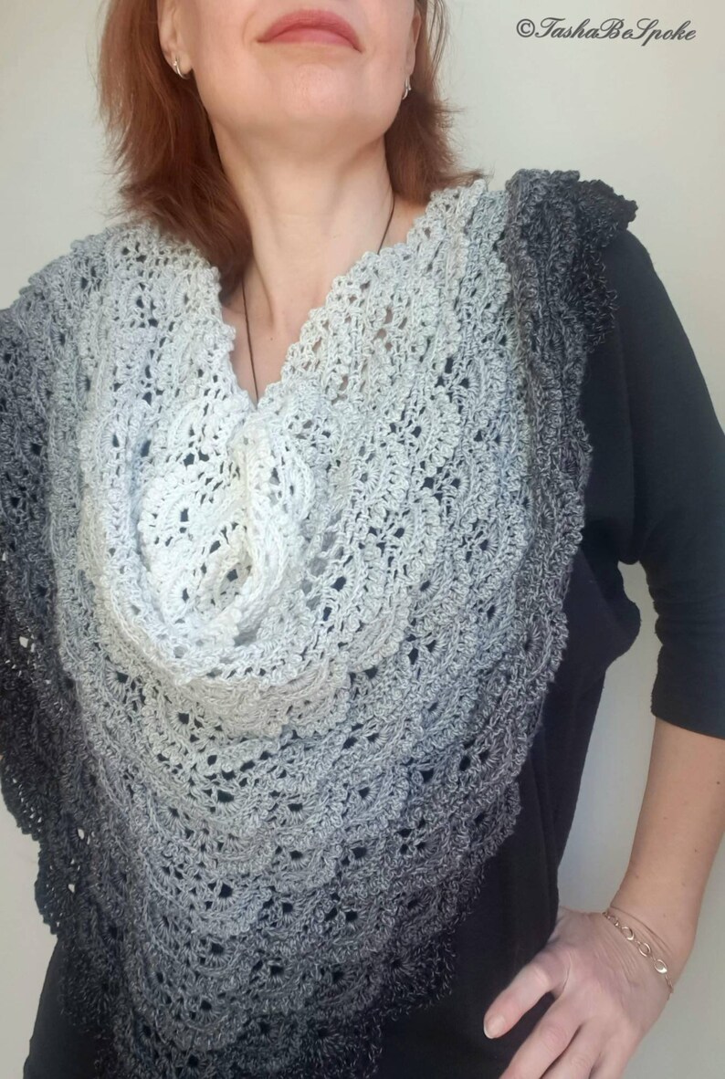 May include: A grey and black crocheted shawl with a scalloped edge. The shawl is draped around a person's shoulders.