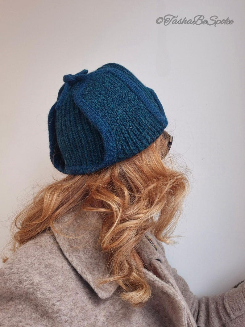 K&ouml;nnte beinhalten: Eine tealblaue Strickm&uuml;tze mit einem einzigartigen gefalteten Design. Die M&uuml;tze ist aus einem weichen, strukturierten Garn gefertigt.