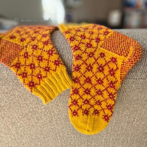 May include: A pair of knitted socks in yellow and red. The socks feature a repeating diamond pattern with red floral accents. The cuffs, heels, and toes are a solid red and yellow. The socks are handmade and appear to be warm and cozy.