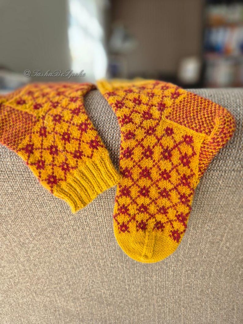 May include: A pair of knitted socks in yellow and red. The socks feature a repeating diamond pattern with red floral accents. The cuffs, heels, and toes are a solid red and yellow. The socks are handmade and appear to be warm and cozy.