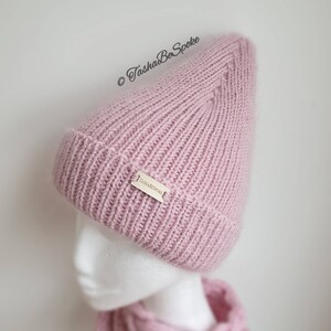 K&ouml;nnte beinhalten: Eine rosafarbene Strickm&uuml;tze mit einem kleinen Etikett mit der Aufschrift "TashaBeSpoke".