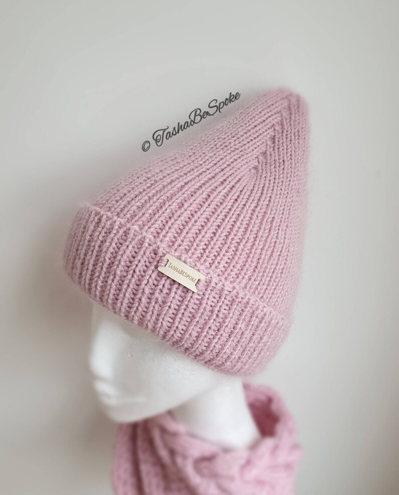 K&ouml;nnte beinhalten: Eine rosafarbene Strickm&uuml;tze mit einem kleinen Etikett mit der Aufschrift "TashaBeSpoke".
