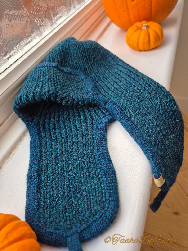 K&ouml;nnte beinhalten: Eine tealblaue Strickm&uuml;tze mit einer langen, spitzen Kapuze. Die M&uuml;tze ist aus dickem, strukturiertem Garn gefertigt und hat ein schlichtes, klassisches Design.