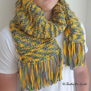 May include: A gray, yellow, and green knitted scarf with long fringe. The scarf is made with a chunky yarn and has a textured pattern.