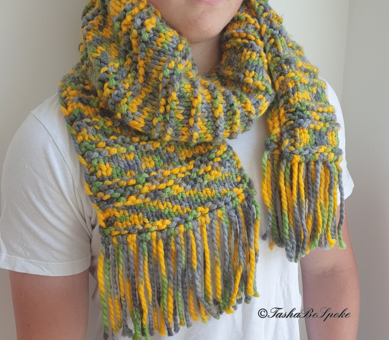 May include: A gray, yellow, and green knitted scarf with long fringe. The scarf is made with a chunky yarn and has a textured pattern.