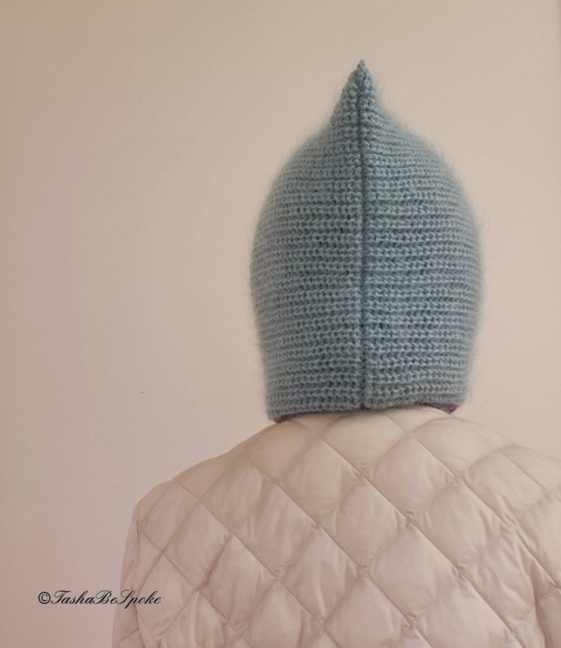 Pu&ograve; includere: Un cappello all'uncinetto blu chiaro a punta. Il cappello &egrave; realizzato con un filato morbido e strutturato e viene indossato sopra una giacca trapuntata bianca. Il design del cappello &egrave; semplice, con una parte superiore a punta e una forma aderente.