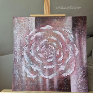 May include: A square canvas artwork depicting a textured rose in pink and white, displayed on a wooden easel. The rose has a raised relief effect. The artist's signature, "TashaBeSpoke", is visible in the upper right corner of the artwork.